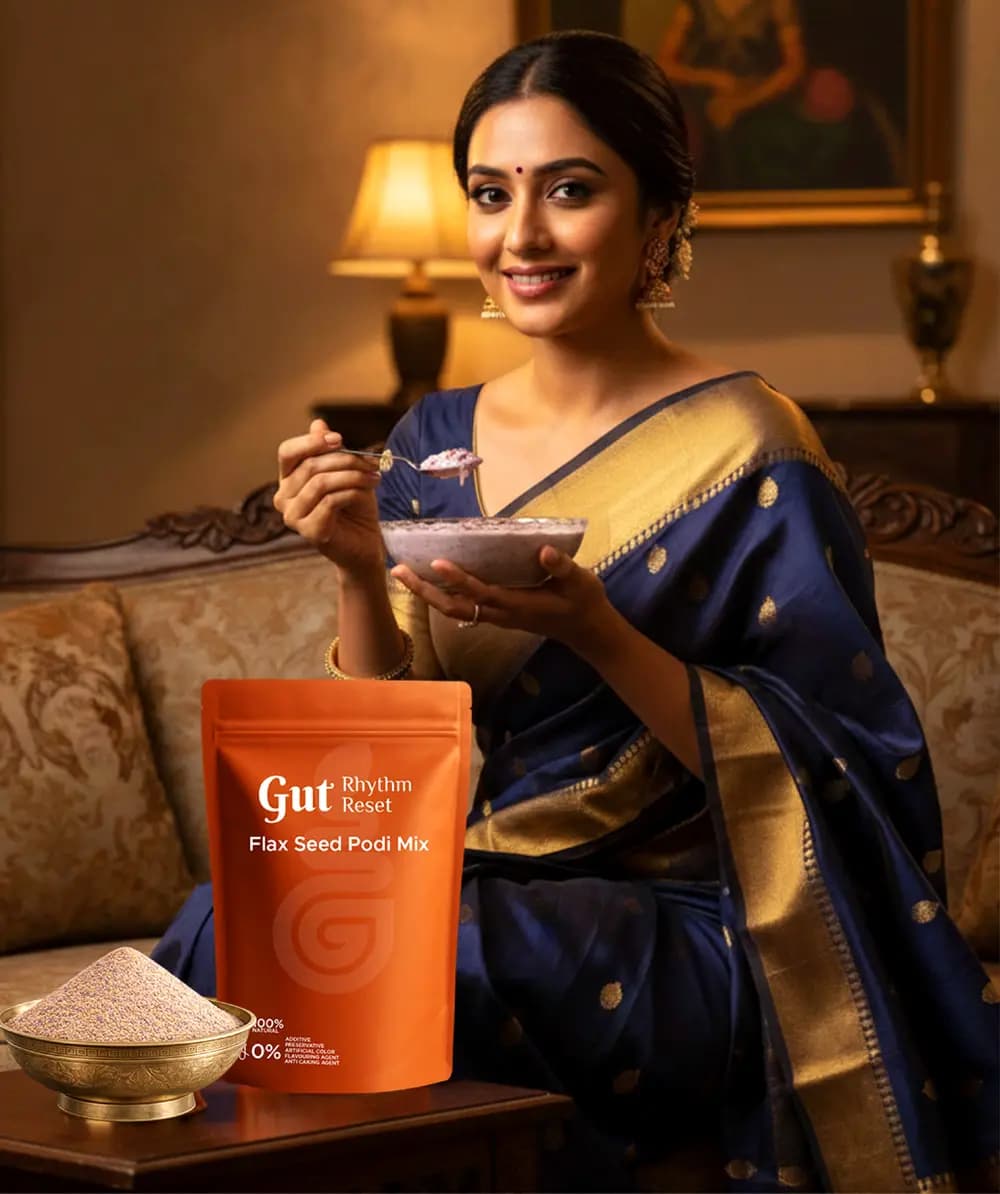 A woman in a navy saree with a bowl of warm Flax Seed Podi, the pouch on the table