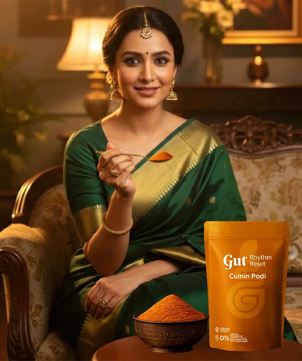 A woman in a green saree with a spoon of Cumin Podi, the pouch and a bowl of podi in front of her